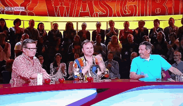a group of people sitting at a table in front of a large crowd with the word wassigb1 on the screen