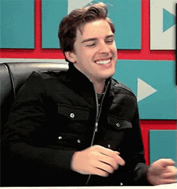 a young man wearing a black jacket is smiling