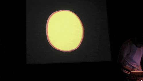 a man stands in front of a large screen with a yellow circle projected on it