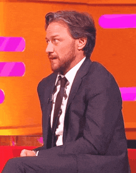 a man in a suit and tie is sitting in front of a pink wall .
