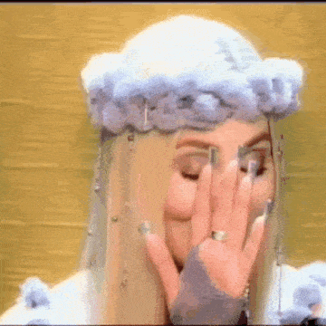 a woman wearing a crown of clouds on her head is covering her face with her hands .