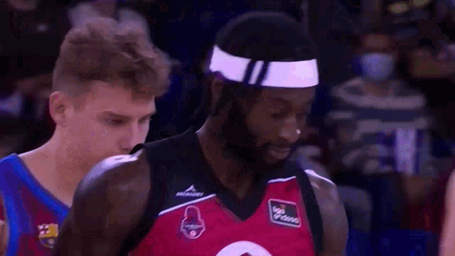 a basketball player with a headband on his head is standing next to another player .