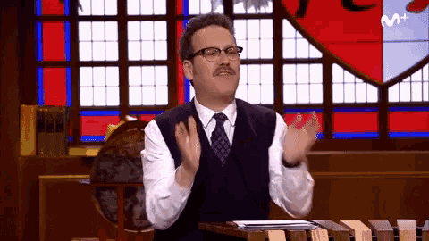 a man in a suit and tie is clapping in front of a stained glass window