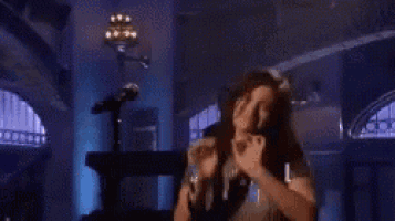 a woman is dancing in a dark room with a man standing in the background .