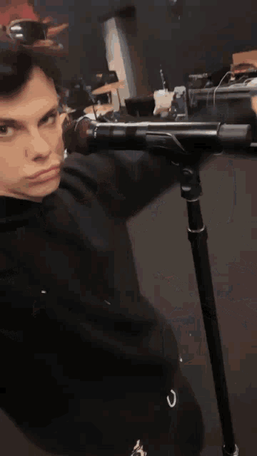 a young man in a black hoodie is standing in front of a drum set .