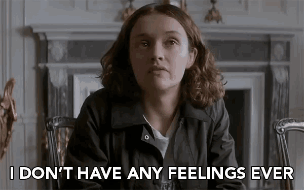 a woman in a black jacket is sitting in front of a fireplace and saying i don 't have any feelings ever .