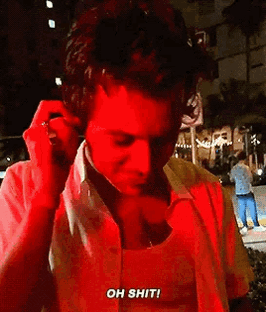 a man in a red shirt is talking on a cell phone while wearing headphones .