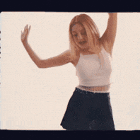 a woman in a white tank top and black skirt is dancing with her arms in the air