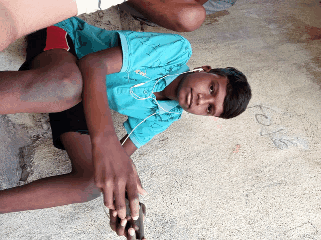 a young boy wearing ear buds sits on the ground looking at the camera