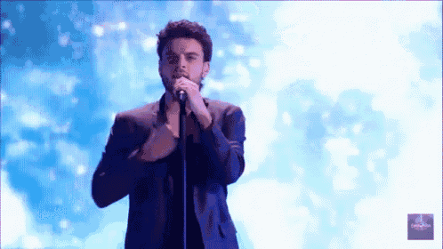 a man in a suit singing into a microphone with a blue background