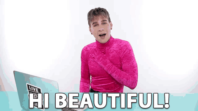 a man in a pink turtleneck says hi beautiful in front of a laptop