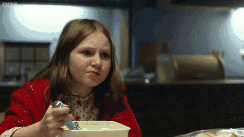 a girl in a red jacket sits at a table with a bbc logo on the bottom