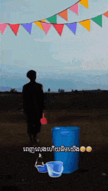 a man is walking in a field with a blue bucket and a bottle of water .
