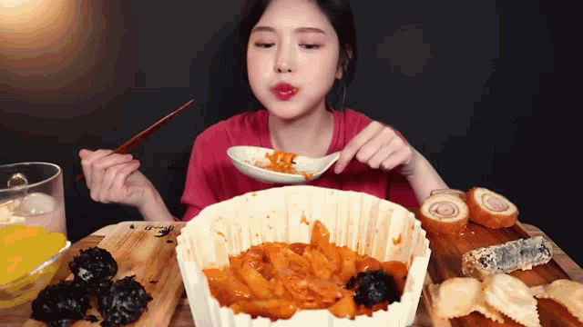 a woman in a red shirt is eating a bowl of food