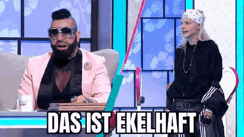 a man in a pink suit and sunglasses is sitting next to a woman in a bandana .