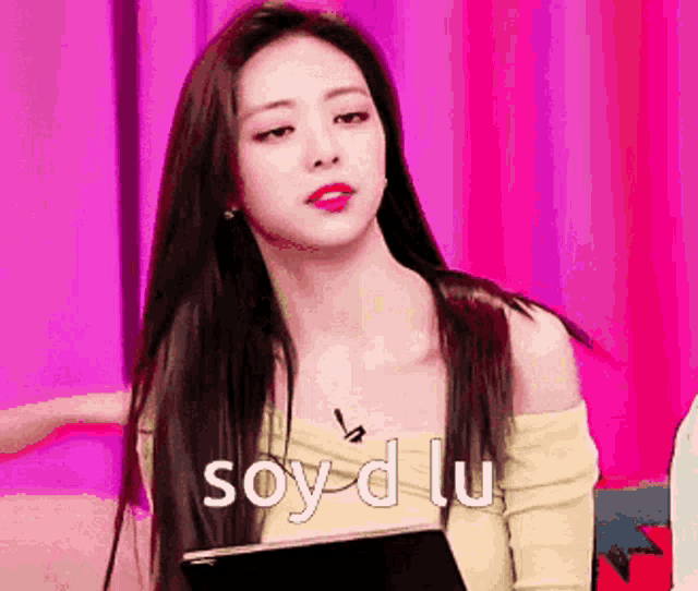 a woman with long hair is sitting in front of a pink curtain and holding a book .