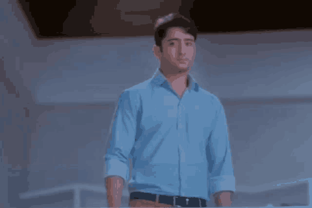 a man in a blue shirt is standing in a room looking at the camera .