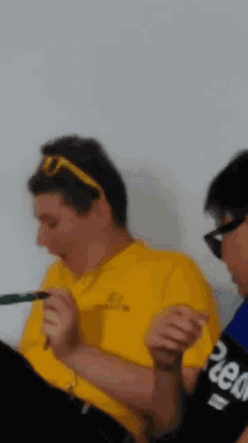 a man in a yellow shirt is holding a pen in his hand
