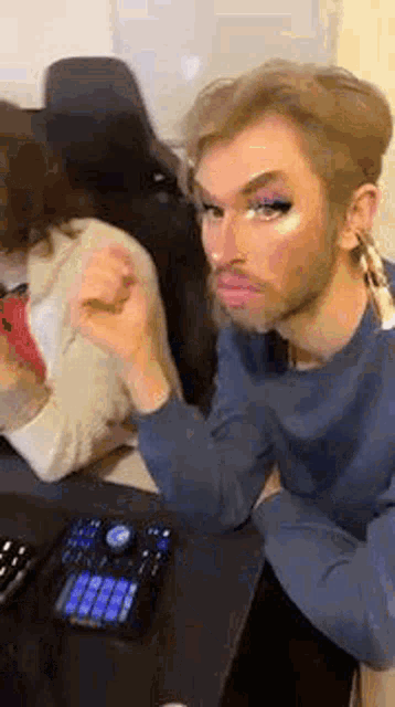 a man with a beard and makeup on his face is sitting at a table with a keyboard .