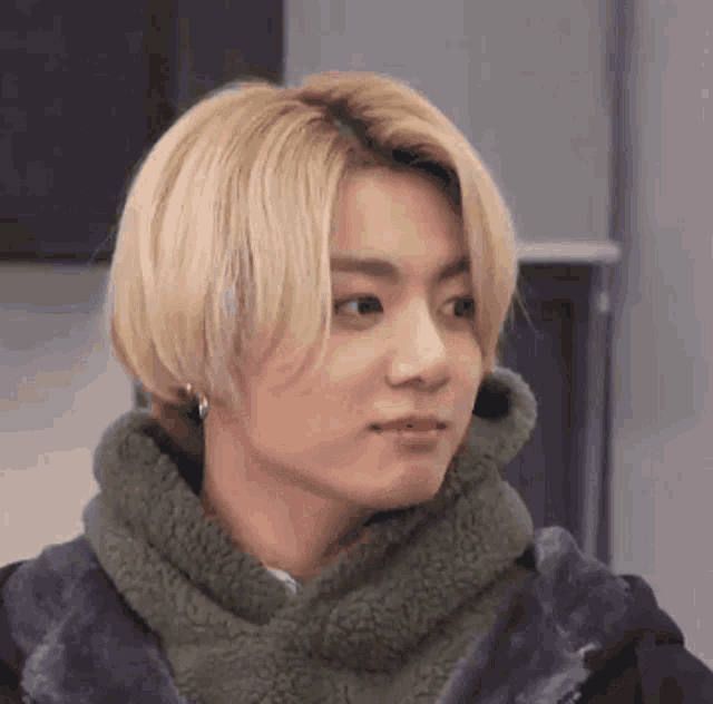 a close up of a person with blonde hair wearing a green scarf and a jacket .