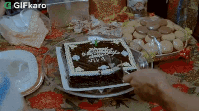 a person is cutting a chocolate birthday cake with a knife .
