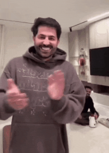 a man wearing a hoodie is standing in a living room and smiling .