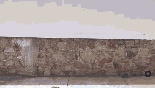 a stone wall with a white roof and a tire on the sidewalk