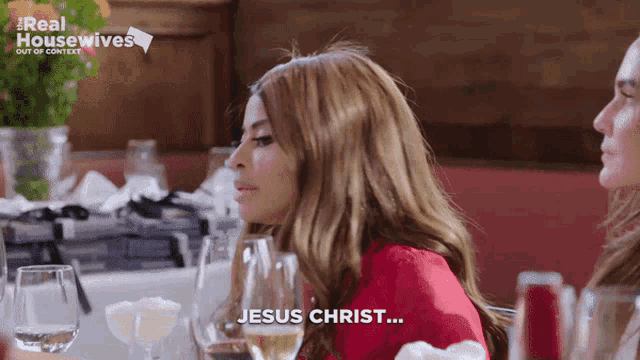 a woman says jesus christ while sitting at a table with wine glasses