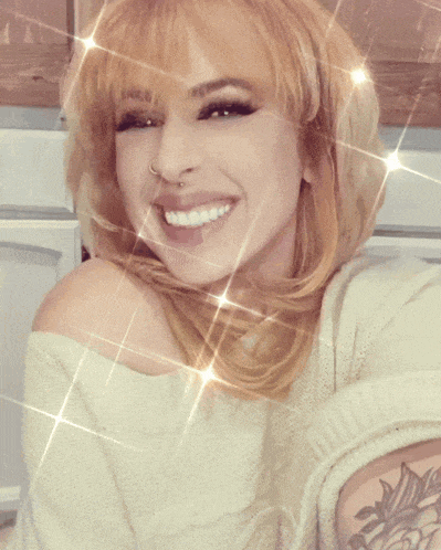 a woman with blonde hair and a tattoo on her arm smiles