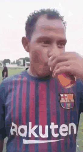 a man wearing a rakuten jersey is drinking a drink from a glass .