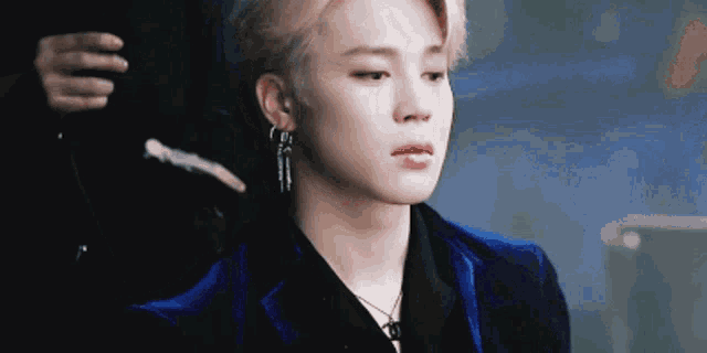 a close up of a young man wearing a blue jacket and earrings