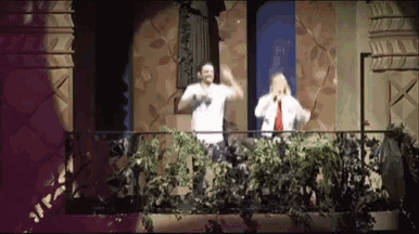 a couple of men standing on a balcony with plants