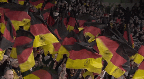 a crowd of people waving german flags in a stadium including one that says ' bundesliga ' on it