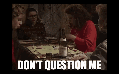 a group of women are sitting at a table playing a board game and one of them is smoking a cigarette .