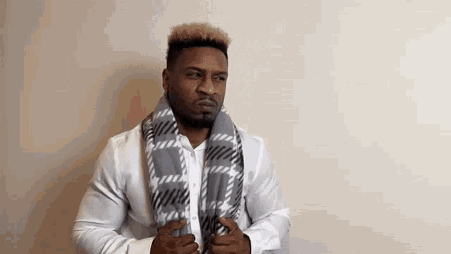 a man wearing a white shirt and a gray scarf is standing in front of a white wall .