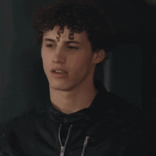 a young man with curly hair wearing a black jacket
