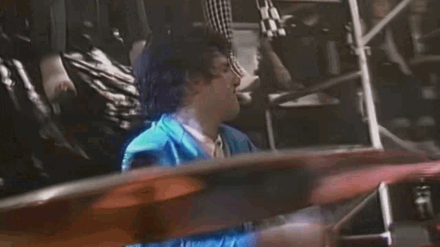 a man in a blue shirt is playing drums in a dark room