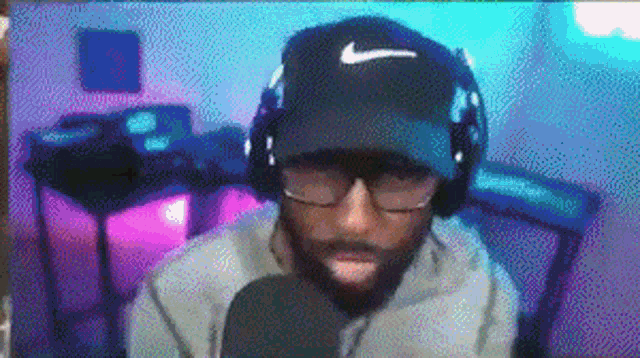 a man with a beard wearing headphones and a hat is talking into a microphone .