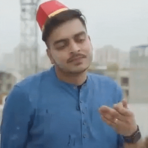 a man wearing a blue shirt and a red hat is eating a chicken .