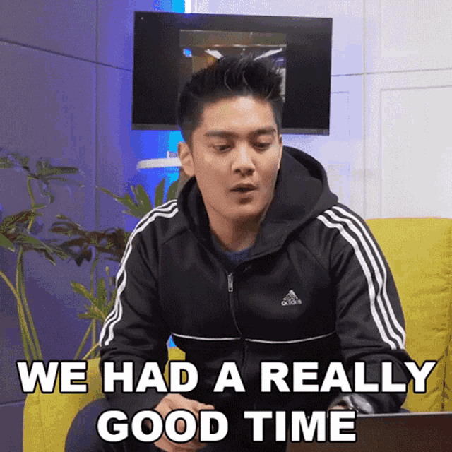 a man wearing an adidas jacket is sitting on a couch with a laptop and says we had a really good time .