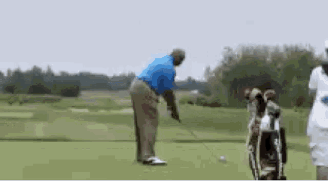 a man is swinging a golf club on a golf course while another person watches .