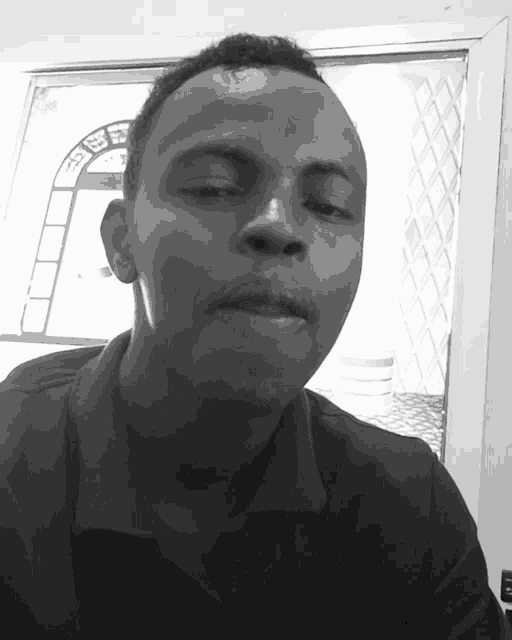 a man 's face is shown in a black and white photo with a window behind him