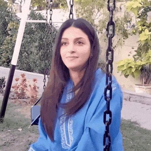 a woman in a blue shirt sits on a chain swing