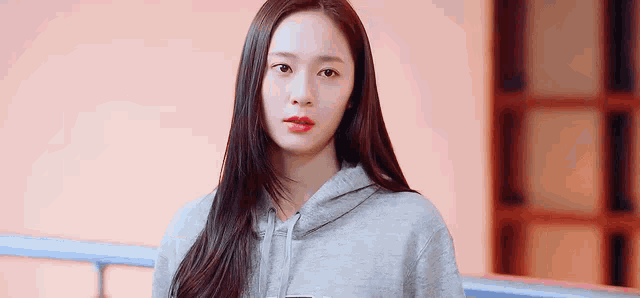 a woman wearing a grey hoodie and red lipstick is looking at the camera .