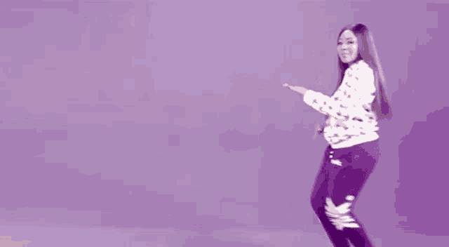 a woman in a white sweater and purple pants is dancing in front of a purple background .