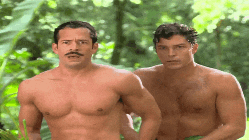 two shirtless men standing next to each other in the woods