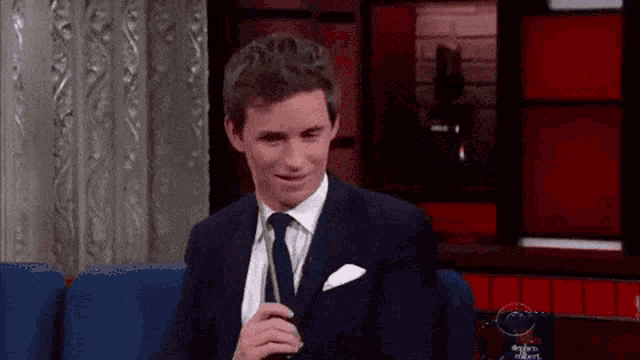 a man in a suit and tie is sitting on a couch holding a glass