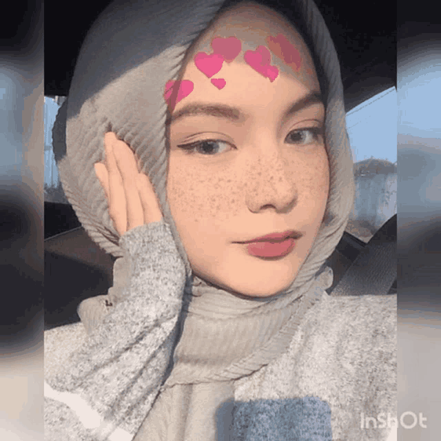 a woman with freckles and hearts on her face is wearing a hijab