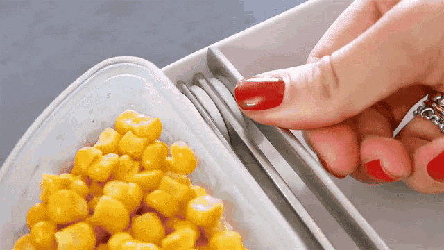 a woman with red nails is holding a container of corn