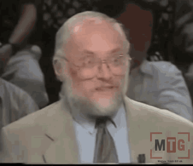 a man with glasses and a beard is sitting in front of a screen that says mug